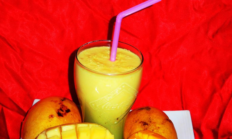 A glass of mango smoothie beside fresh mango pieces.